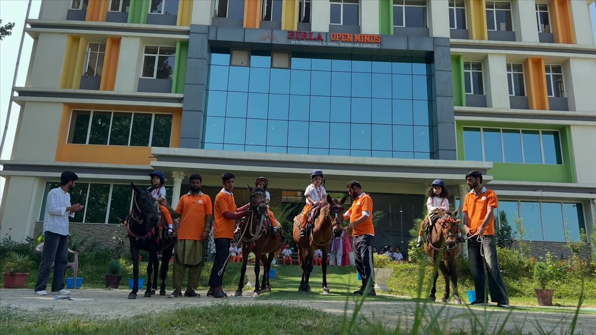 Young students on horseback with trainers in front of Birla Open Minds International School, HMT Srinagar